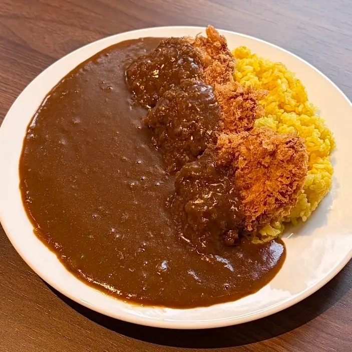 ひとくちチキンカツをのせたカレー。ターメリックライスと一緒に白い皿で