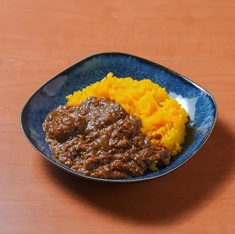 深い茶色に煮込んだ牛すじカレー。ターメリックライスを添えて青い皿に