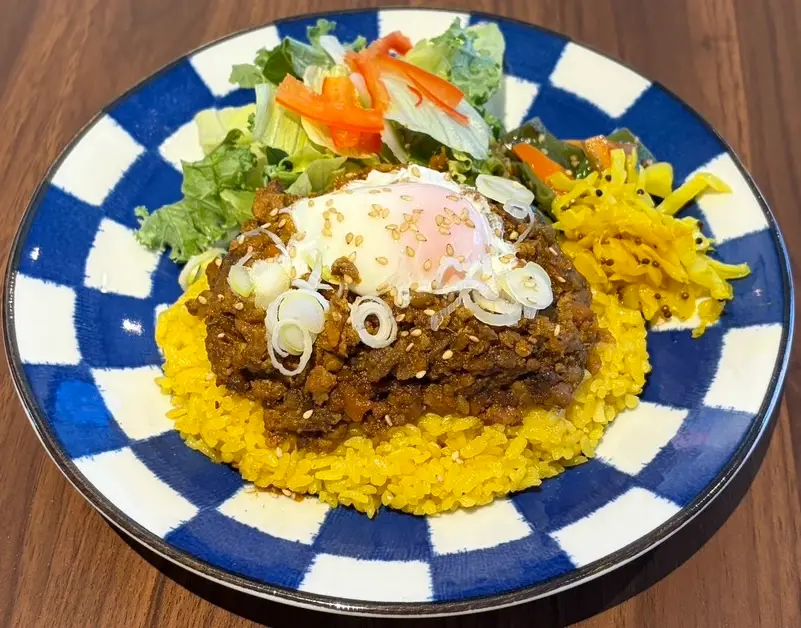 温玉と白髪ねぎをのせた和風キーマカレー。ターメリックライスとサラダ添え