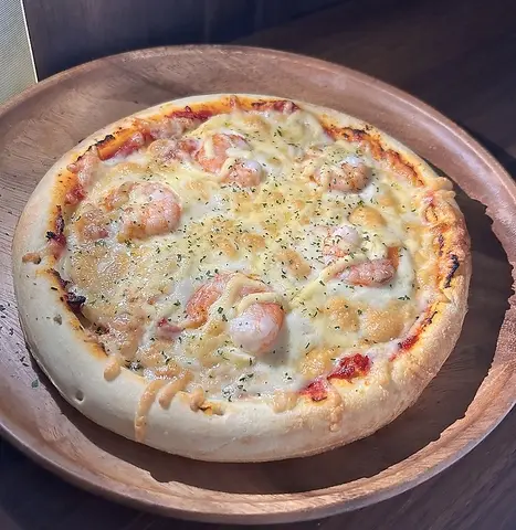 えびとチーズにパセリを振ったエビマヨピザ。木の皿に